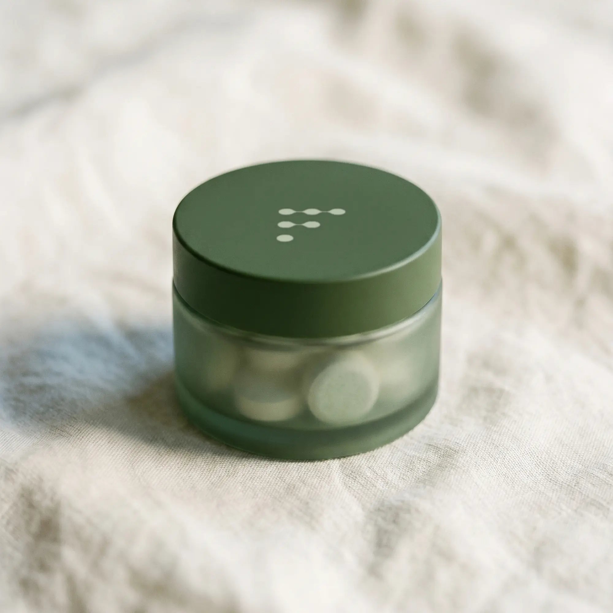A small Fenn Method travel jar resting in an open palm, on cream linen.